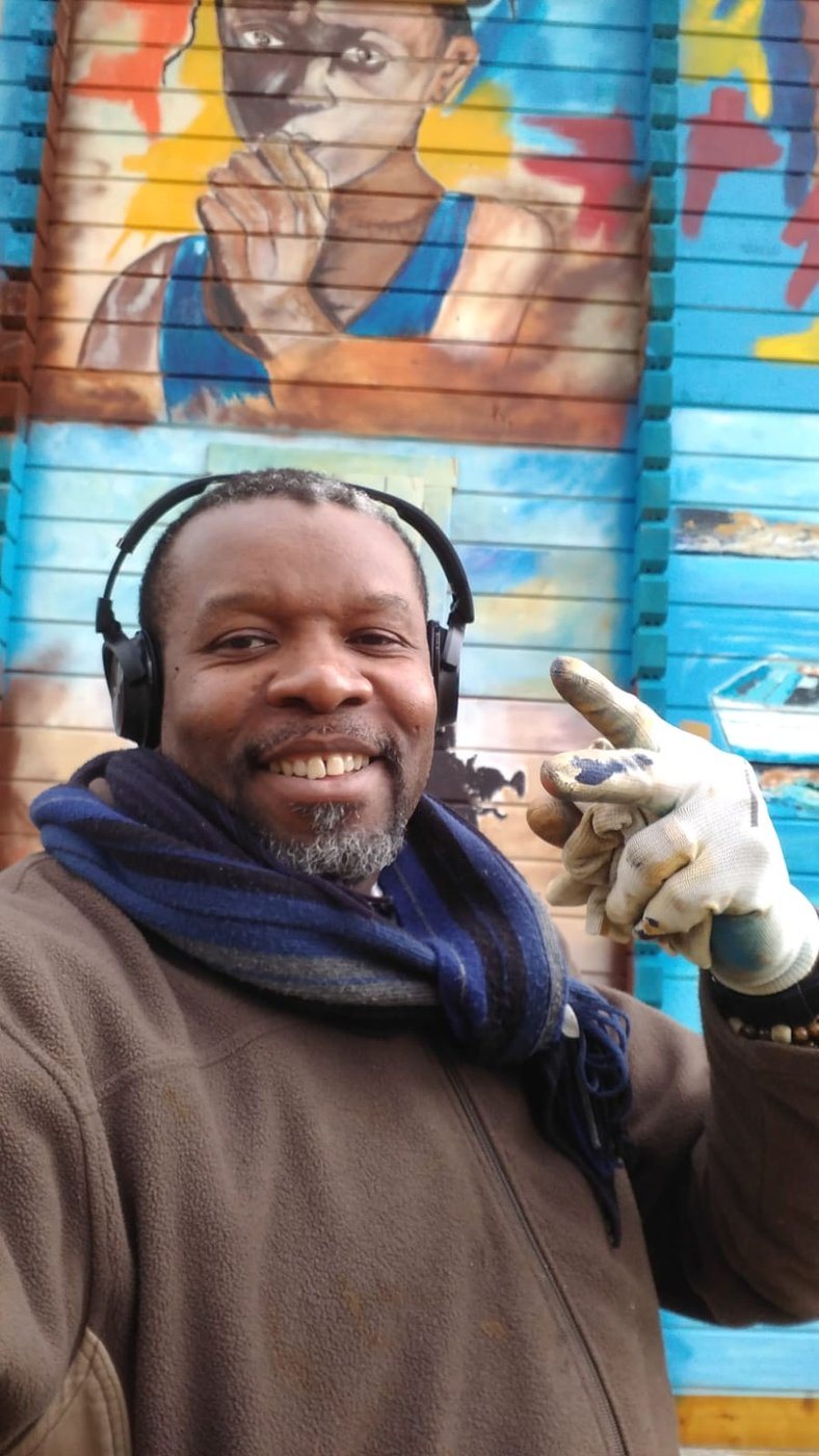 Vincenzo Follykoué souriant devant une fresque peinte