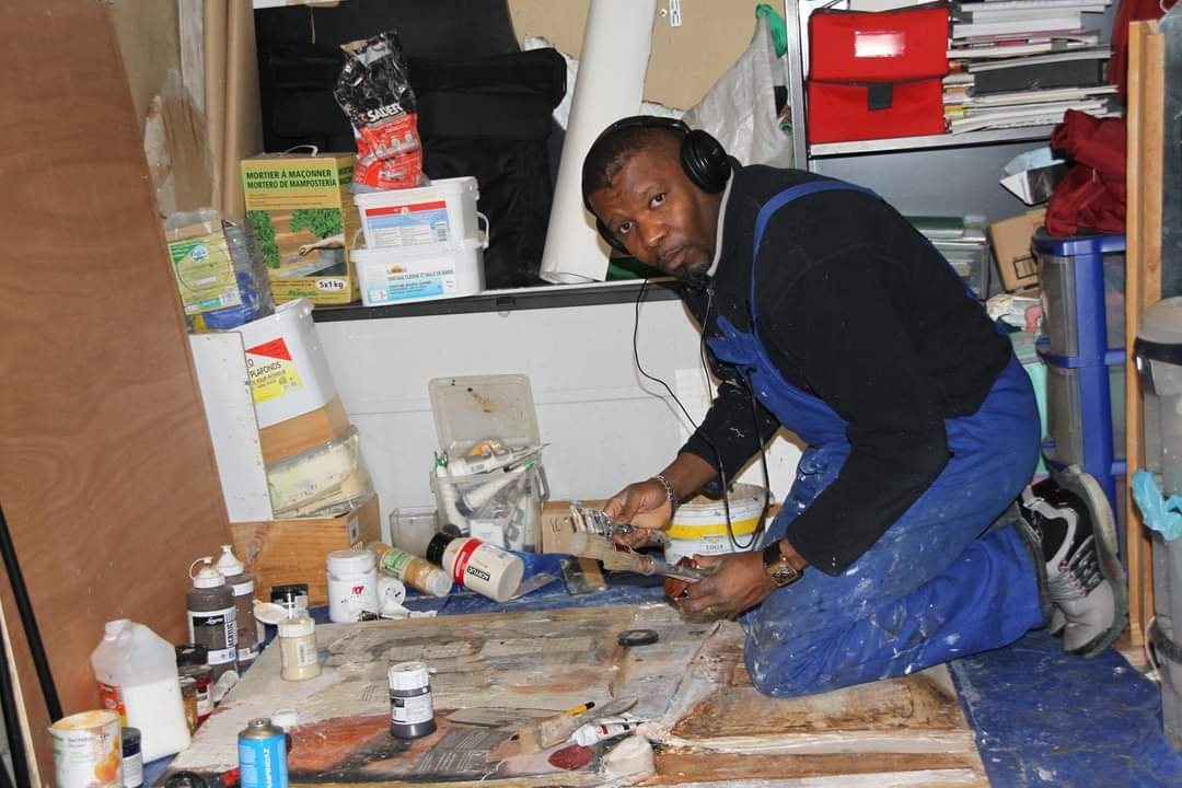 Vincenzo Follykoué à genoux dans son atelier, travaillant une toile posée au sol